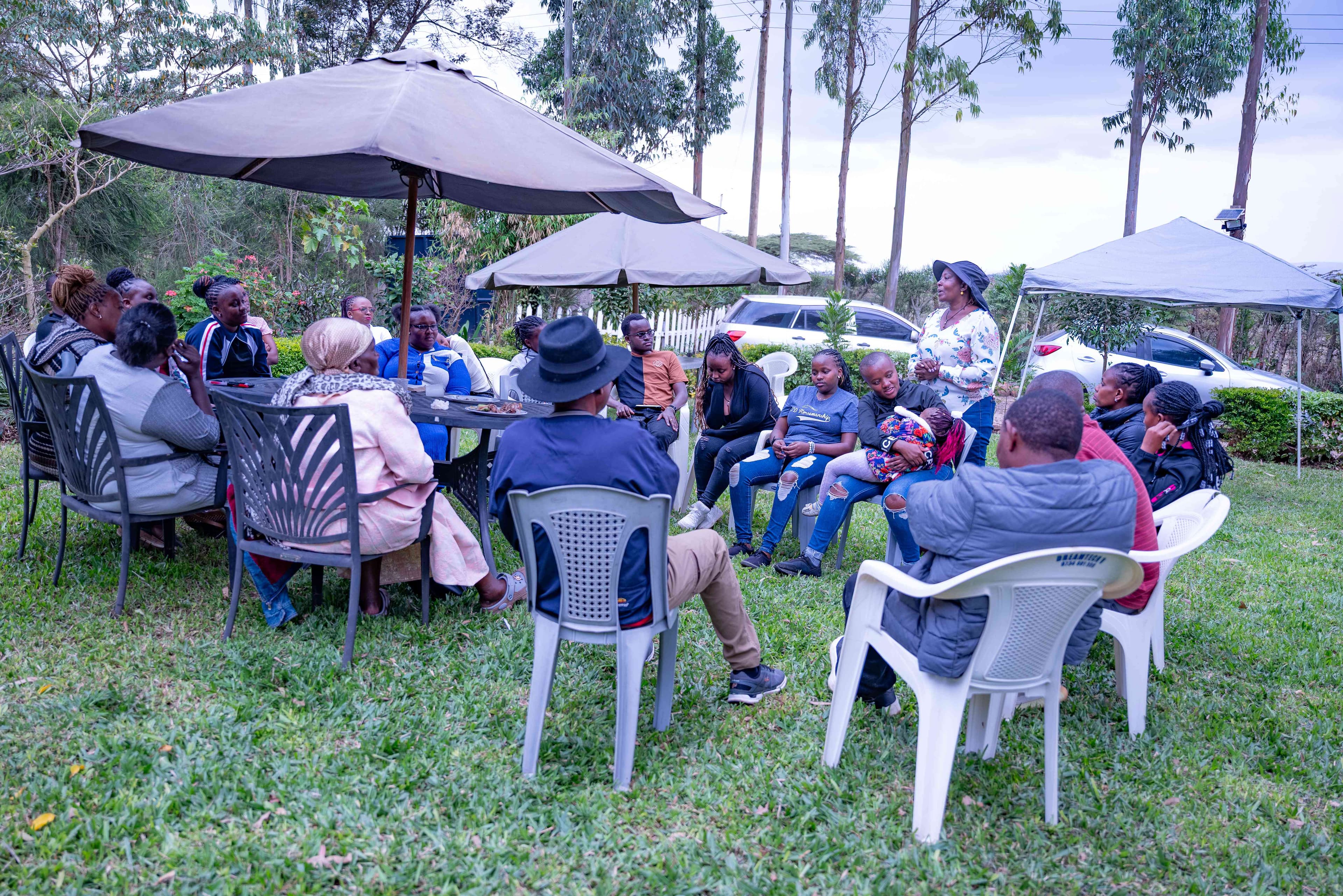Intimate group discussion session with participants seated in a circle under umbrellas, engaged in meaningful conversation on the farm grounds